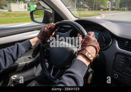Ein Mann mit braunen Lederhandschuhen, der ein modernes Auto lenkt, das aus dem Inneren des Fahrzeugs entnommen wurde Stockfoto