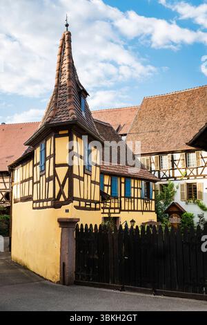 Schmales gelbes Fachwerkhaus mit spitzem Dachgiebel am Eingang eines Winzers in der historischen Altstadt von Eguisheim, Elsass, Frankreich Stockfoto