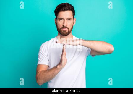 Junger selbstbewusster bärtiger Mann in weißem T-Shirt, der eine Auszeit-Geste vor türkisfarbenem Hintergrund macht Stockfoto