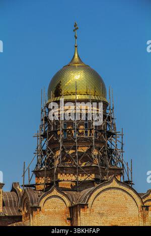 Ein detaillierter Blick auf eine goldene Kuppel auf einer orthodoxen Kirche, die gerade restauriert wird, umgeben von Holzgerüsten vor einem klaren blauen Himmel. Stockfoto