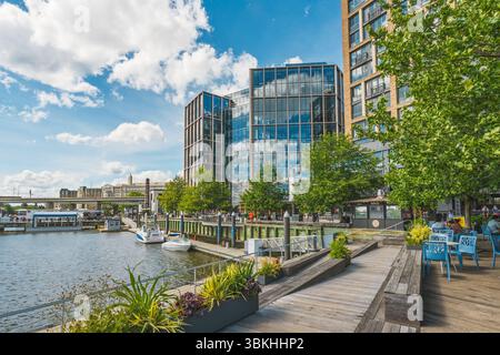 Washington D.C., USA - 24. Mai 2025. Fußgänger genießen einen entspannten Spaziergang entlang des Flusses mit modernen Glasgebäuden, die den Himmel reflektieren. Stockfoto