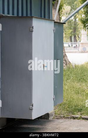 Eine Außenaufnahme eines verwitterten, grauen Metallschaltkastens in einem Park, gesichert mit einem hellblauen Vorhängeschloss, zeigt die Versorgungsinfrastruktur und Stockfoto