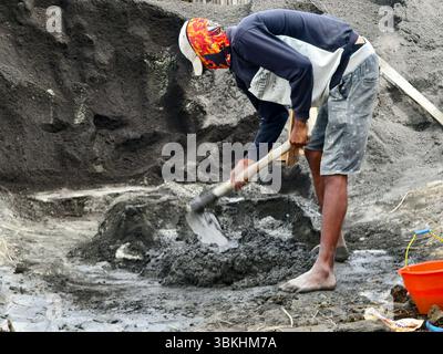 Badung, Bali, Indonesien – 19. Juni 2025: Ein Bauarbeiter mischt Zement oder Mörtel manuell mit einer Schaufel Stockfoto