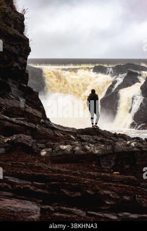 Eine Frau, die von hinten gesehen wird, steht vor den mächtigen Chaudière Falls und fängt einen Moment der Ehrfurcht in der Natur ein. Stockfoto