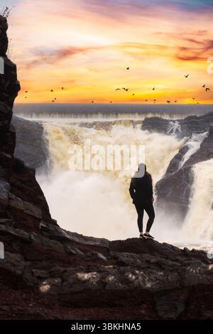 Eine Frau, die von hinten gesehen wird, steht vor den mächtigen Chaudière Falls und fängt einen Moment der Ehrfurcht in der Natur ein. Stockfoto