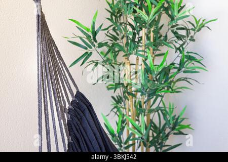 Entspannende Innenecke mit Hängematte und dekorativer Bambuspflanze im Topf. Stockfoto