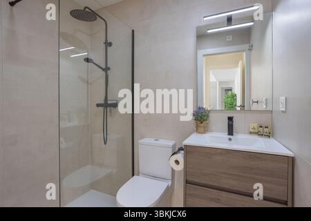 Modernes Bad mit bodenebener Glasdusche, Holzwaschtisch und großem Spiegel mit Beleuchtung. Stockfoto