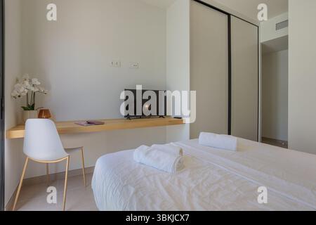 Einfaches und sauberes Schlafzimmer mit weißer Bettwäsche, Flachbildfernseher und verschiebbarem Kleiderschrank. Stockfoto
