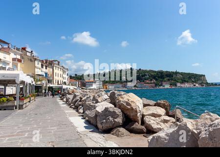 PIRAN, SLOWENIEN - 19. MAI 2025: Ein malerischer Panoramablick fängt die atemberaubende Küste von Piran, Slowenien, unter einem hellblauen Himmel mit Streuung ein Stockfoto