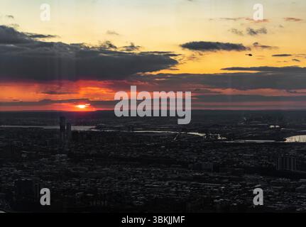 Das Bild erfasst eine atemberaubende Luftaufnahme einer Stadt, während die Sonne hinter einem bewölkten Himmel untergeht und ein warmes Orange über die urbane Landschaft strahlt. Die Stockfoto