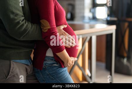 Zärtlicher Moment, der Ehemann umarmt liebevoll den Bauch seiner schwangeren Frau, während sie Zeit miteinander verbringen Stockfoto
