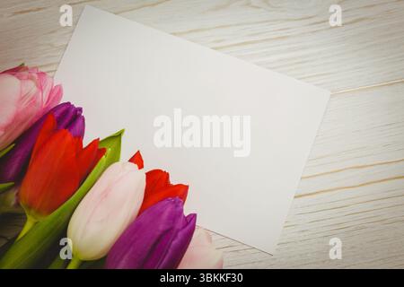 Flache weiße Grußkarte mit flachem Design liegt schräg auf Holztisch mit Tulpen, Kopierraum Stockfoto