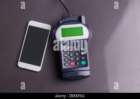 Das flache Design zeigt die Tastatur des Smartphones und der Kartenterminals auf der dunkelgrauen Tischplatte Stockfoto