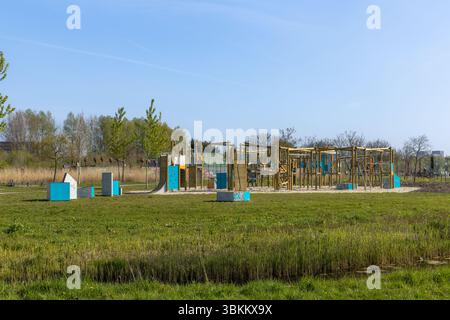 Farbenfrohe Holzspielplatz-Struktur mit verschiedenen Kletter- und Spielelementen an einem sonnigen Tag in einer Parklandschaft. Stockfoto