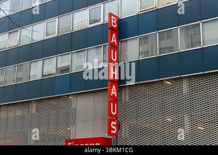 Ein hohes, graues Bauhausgebäude mit einem vertikalen roten Schild mit dem Firmennamen. Moderne Architektur und Einzelhandelskonzept. Berlin, Deutschland. 29. März Stockfoto