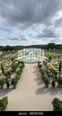 Blick von oben auf einen sorgfältig gepflegten formellen Garten mit symmetrischen Mustern, einen runden Teich und ein entferntes Gewässer unter einem bewölkten Himmel. Stockfoto