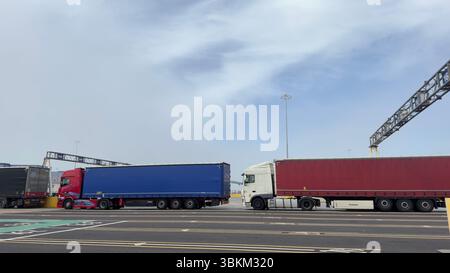 Mehrere Sattelauflieger parkten in einer Reihe unter bewölktem Himmel, mit sichtbaren Deckenkonstruktionen und Straßenmarkierungen. Stockfoto
