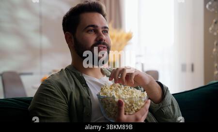 Glücklicher entspannter kaukasischer bärtiger Geschäftsmann männlicher Geschäftsmann Geschäftsmann Hauseigentümer Kunde sitzt Sofa zu Hause essen Snack Popcorn Schüssel Fernsehen Stockfoto