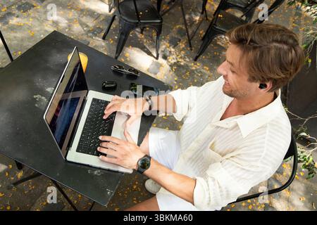 Freelancer mit Laptop auf der Terrasse des Coffee-Shops, Blick von oben junger Mann, der an einem Laptop arbeitet Stockfoto