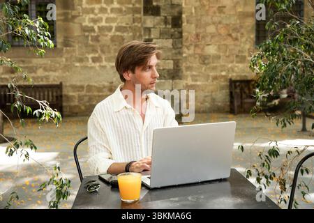 Portraitprofil eines Modellmannes mit Computer. Arbeiten und entspannen Sie im sonnigen Stadtcafé Stockfoto