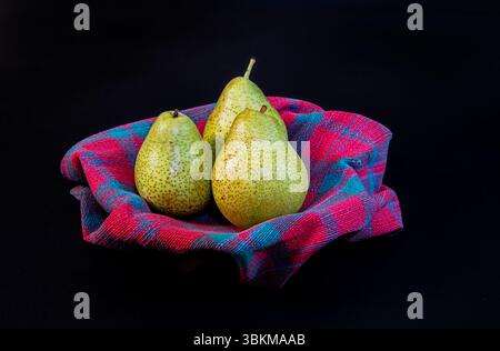Drei reife Birnen ruhen elegant in einer Schüssel auf schwarzem Hintergrund und betonen ihre natürliche Textur und lebendige Farbe in dramatischer Beleuchtung. Stockfoto