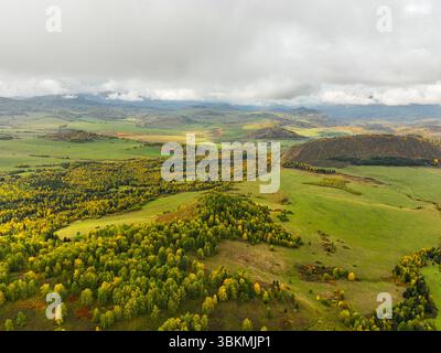 Eine atemberaubende Aussicht aus der Vogelperspektive auf eine weitläufige Herbstlandschaft mit lebhaften gelben und grünen Wäldern, sanften Hügeln und fernen Bergen Stockfoto