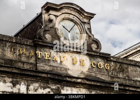 Chateau de Cognac' in goldenen Buchstaben: Erbaut als mittelalterliche Festung, bedeutende Renaissance-Residenz unter Francois I. und Wiege des französischen Königs - symbolisiert die Transformation der Region: Vom Sitz der Macht zum Zentrum der Cognac-Produktion. Die Mauern erzählen sowohl von der königlichen Geschichte als auch von der Geburt eines der berühmtesten Geister Frankreichs. Fassade der Burg „Château de Cognac“ mit einer alten Uhr und dem Namen der Burg in goldenen Buchstaben. Die Uhr zeigt die Zeit und ist ein historisches Detail des Gebäudes. Boulevard Denfert Rochereau, Cognac, Nouvelle-Aquitaine, Frankreich Stockfoto