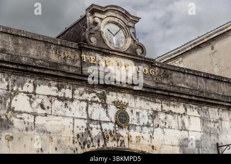Haupteingang zum Cognac Castle. Das Gebäude wurde 1797 von Baron Otard übernommen, der hier die berühmte Cognac-Marke gründete. Die dicken Burgmauern boten ideale Lagerbedingungen. Heute ist das imposante Gebäude nicht nur ein Denkmal der französischen Geschichte, sondern auch ein aktives Cognachaus, das Führungen und Einblicke in die Produktion des Geistes bietet. Fassade der Burg „Château de Cognac“ mit einer alten Uhr und dem Namen der Burg in goldenen Buchstaben. Die Uhr zeigt die Zeit und ist ein historisches Detail des Gebäudes. Boulevard Denfert Rochereau, Cognac, Nouvelle-Aquitaine, Frankreich Stockfoto