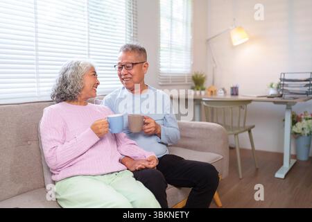 Ein älteres asiatisches Paar teilt sich einen zärtlichen Moment zu Hause und genießt Kaffee und die Gesellschaft des anderen. Dieses Bild fängt das Wesen lebenslanger Liebe und p Stockfoto