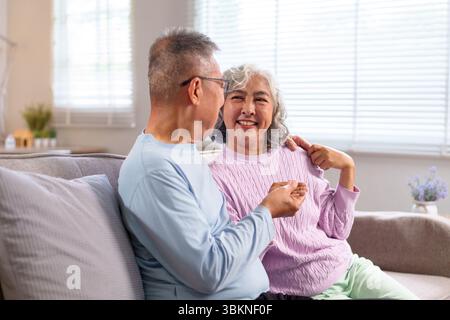 Dieses herzerwärmende Bild zeigt ein älteres asiatisches Paar, das in seinem gemütlichen Zuhause gute Zeit zusammen verbringt, um das Altern zu feiern und die Gesellschaft in sich zu nehmen Stockfoto