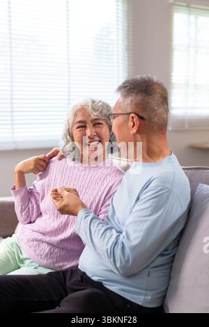Ein glückliches älteres asiatisches Paar teilt einen besonderen Moment auf dem Sofa und sieht sich mit Liebe und Zuneigung an. Sie genießen ihre gemeinsame Zeit in Stockfoto