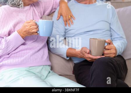 Dies ist ein Porträt von Händen, die eine Tasse warmes Getränk halten. Das ältere Paar verbringt Zeit zusammen, um sich zu Hause zu entspannen. Es ist ein besonderer Moment der Re Stockfoto