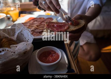Eine Person genießt einen Moment der kulinarischen Genüsse, indem sie eine reichhaltige Tomatensoße auf geröstetem Brot während eines ruhigen Frühstücks verteilt. Die Umgebung strahlt Wärme aus Stockfoto