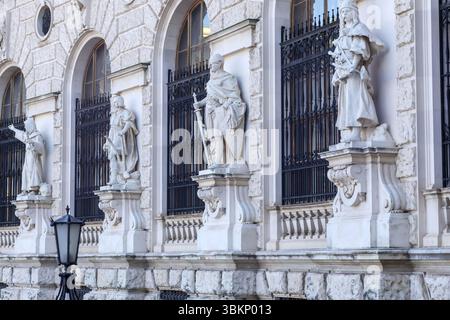 Die Fassade eines klassizistischen Gebäudes mit mehreren weißen Statuen in Nischen zwischen Fenstern mit dunklen Metallstangen und einer altmodischen Straßenlampe Stockfoto