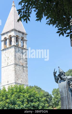 SPLIT, KROATIEN, 08.06.2018: Eine ruhige Szene mit einem historischen Glockenturm neben einer hohen Statue, umgeben von üppigem Grün, unter einem klaren blauen Himmel, Stockfoto
