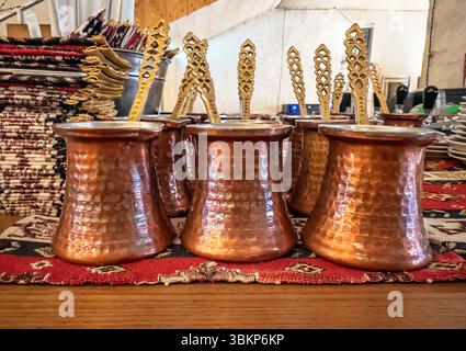 Traditionelle türkische Kaffeekannen aus gehämmertem Kupfer (Cezve) mit verzierten Messinglöffeln, ausgestellt auf einem farbenfrohen ethnischen Teppich. Nahaufnahme aus authentischem Kupfer Stockfoto