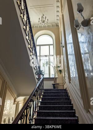 Elegantes Interieur eines Luxushauses mit einer Marmortreppe und einem großen Bogenfenster. Pracht klassischer Architektur: Eine majestätische Treppe mit Stockfoto