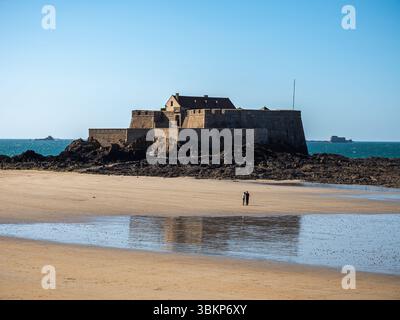 Sehen Sie sich das Fort National aus dem 17. Jahrhundert von Vauban in Saint-Malo an, mit einem Paar, das bei Ebbe spazieren geht. Historische Küstenverteidigung in der Bretagne, Fran Stockfoto