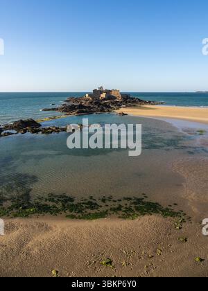 Vertikaler Blick auf Fort National in Saint-Malo, Bretagne, Frankreich, bei Ebbe mit sandigen Pools, Felsen und klarem blauem Himmel im Abendlicht. Stockfoto