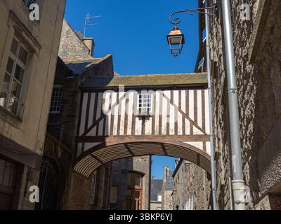 Fachwerkbau mit Bogengang, der zwei Häuser oberhalb einer Kopfsteinpflasterstraße in der Altstadt von Saint-Malo, Bretagne, an einem sonnigen Tag verbindet. Stockfoto