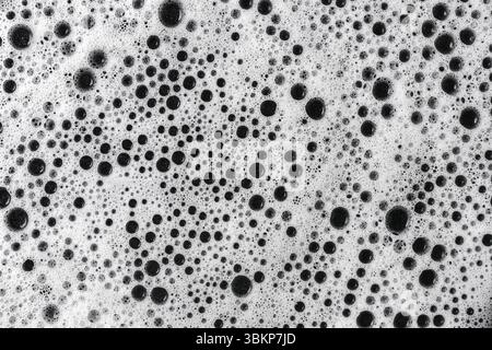 Dichter Schaum mit schwarzer Blasenstruktur. Reinigungsmitteloberfläche Nahaufnahme. Hygiene- und Waschhintergrund mit abstrakten Kreisblasen. Stockfoto