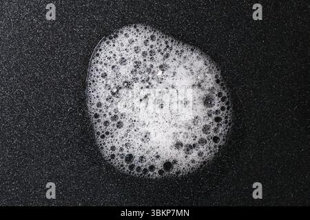 Weiße Seifenschaumblase auf schwarzem Hintergrund. Abstraktes Reinigungskonzept mit Waschmittelstruktur. Nahaufnahme von Suds mit glänzender Oberfläche. Stockfoto