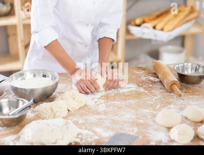 Niedliche Teige auf dem Tisch in der Bäckerei mit Nahaufnahme von Frauenhänden, die gekonnt Teig an der Lebensmittelproduktionslinie kneten Stockfoto