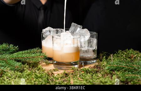 Elegante Whiskey-Cocktails mit Eis und Sahne werden in einer rustikalen Bar mit Moos- und Kiefernbedeckung in einer von der Natur inspirierten Umgebung serviert. Stockfoto