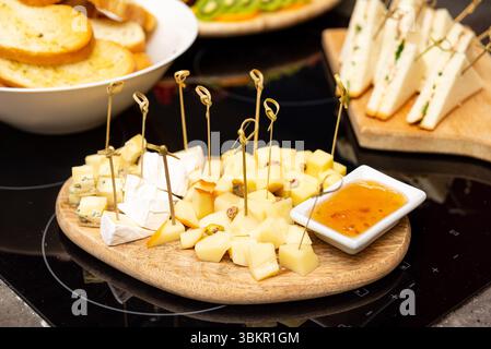 Elegantes Holzkäsebrett mit gemischten Käsewürfeln, Pistazien und Marmelade, perfekt für Wein oder Vorspeisen. Stockfoto