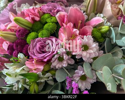 Detaillierte Ansicht eines lebendigen Blumenstraußes mit rosa Lilien, lila Rosen, grünen Chrysanthemen, Gänseblümchen und Eukalyptusblättern – perfekt für Blumendesign Stockfoto