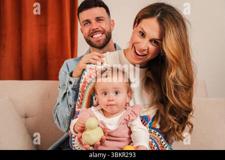 Glückliche Familie, die wertvolle Momente genießt, während sie mit ihrem entzückenden Baby und ihren farbenfrohen Spielzeugen in einer gemütlichen Umgebung voller Wärme und Liebe interagiert Stockfoto