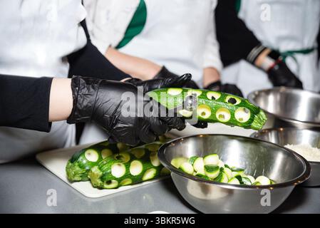 Nahaufnahme von Köchen, die mit Melonenballern frische Zucchinis aushohlen und Gemüse für das Kochen in einer professionellen Küche zubereiten. Stockfoto
