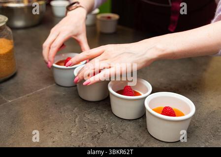 Handauflage für individuelle Himbeer-Panna-Cotta-Desserts in weißen Ramekins, perfekt für elegante Veranstaltungen und Catering-Menüs. Stockfoto