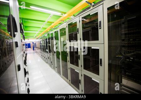 Serverschränke mit Glasfront säumen einen flachen Rechenzentrumskorridor mit gelben Kabeltrassen Stockfoto